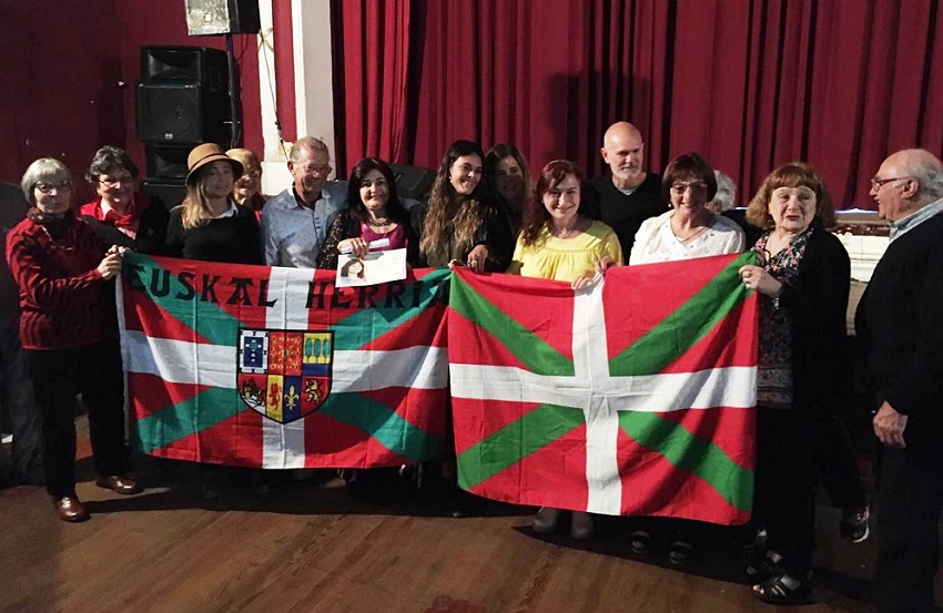 Monica Arrazubieta behind the Ikurriña with certificate in hand, surrounded by family and friends who attended the event