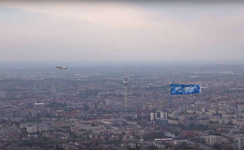 The airplane and banner with the skies of Gernika flying over Alexanderplatz, the epicenter of the German capital